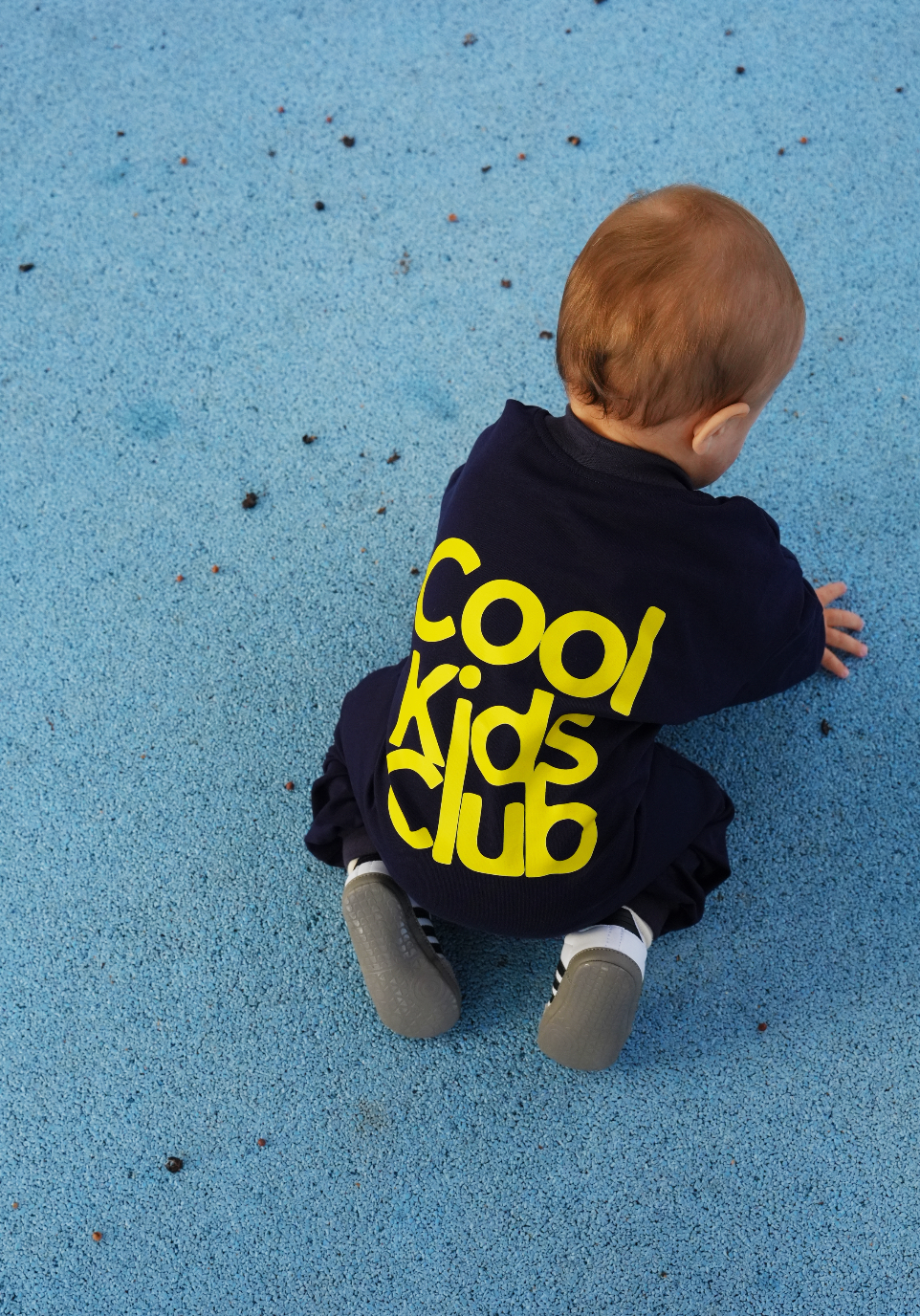 Bébé à quatre pattes en combinaison bébé oversize bleu marine, flocage Cool Kids Club jaune au dos